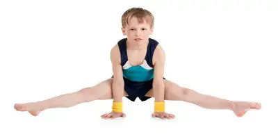 A young boy is doing the splits in his gym clothes.